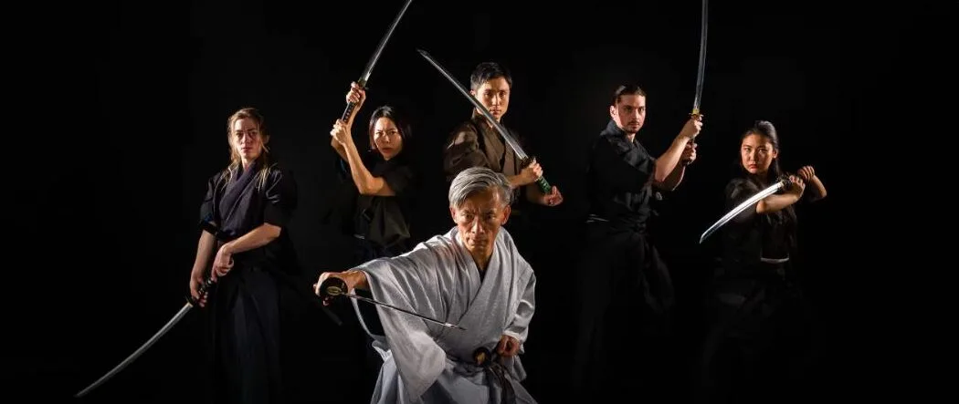 The Samurai Sword Soul cast in stage costume with drawn swords, lit against a black background