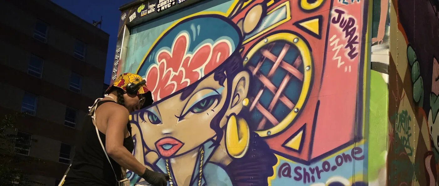 Shiro One spray-painting a mural at Showdown Chinatown, with Juraku tagged on the wall