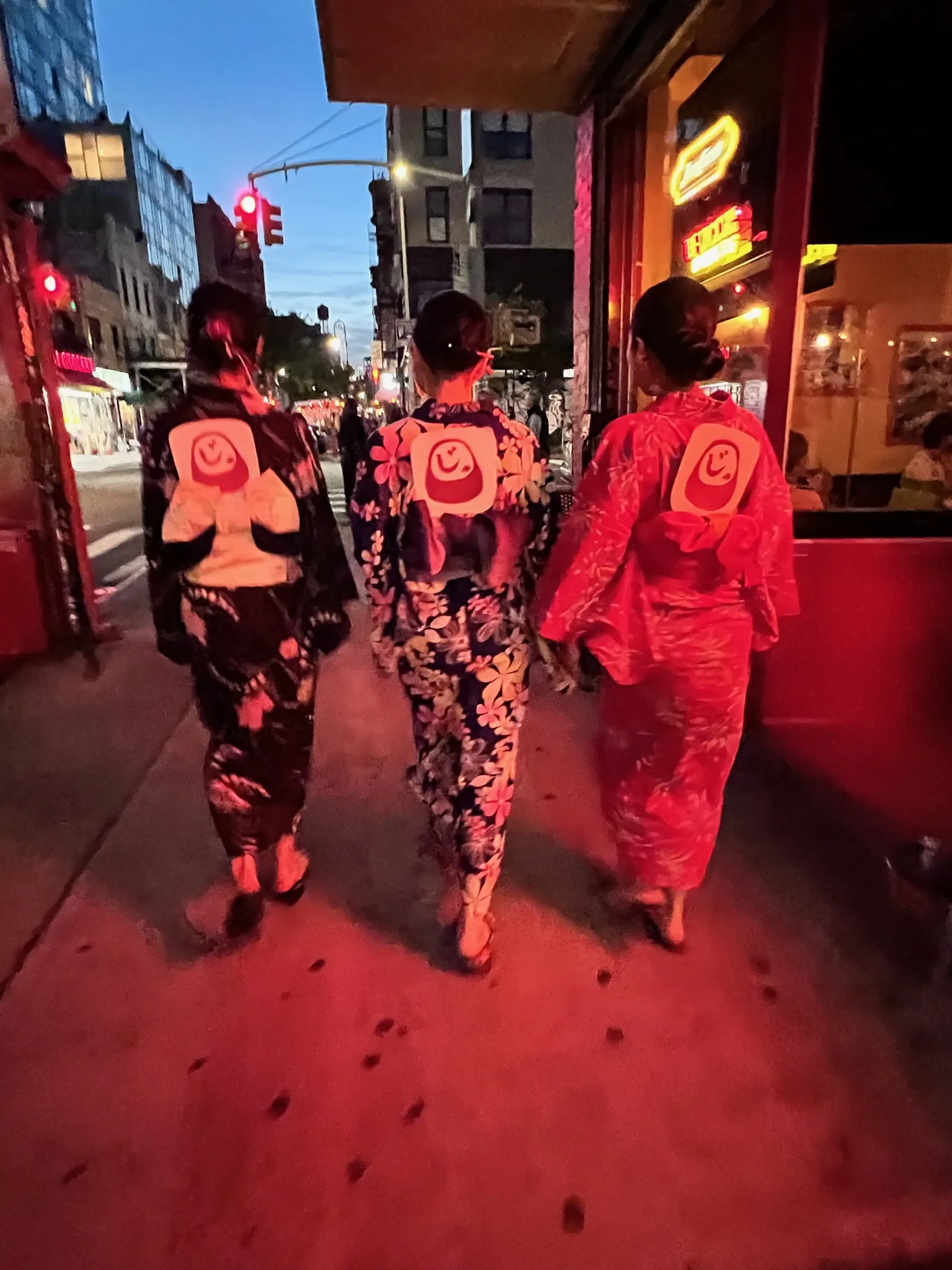 Guests in yukata walking past Izakaya Juraku's neon-lit storefront on Ludlow Street at night